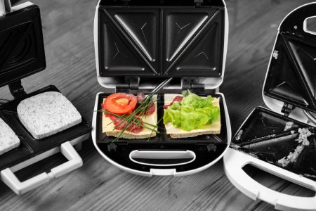 Téléchargez les photos : Sandwichs appétissants avec jambon et herbes dans un fabricant de sandwich sur un fond noir et blanc. - en image libre de droit