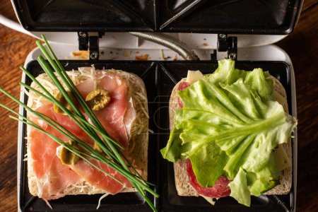 Téléchargez les photos : Faire des sandwichs à partir de jambon, légumes et fromage dans une machine à sandwich. Deux toasts avec des garnitures différentes close-up. - en image libre de droit