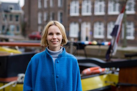 Téléchargez les photos : Femme adulte en manteau souriant tout en voyageant aux Pays-Bas. Voyages et aventures agréables. Une personne positive. - en image libre de droit