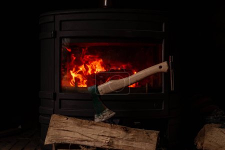 Axe with log on background of burning fireplace. Wood heating, firewood concept