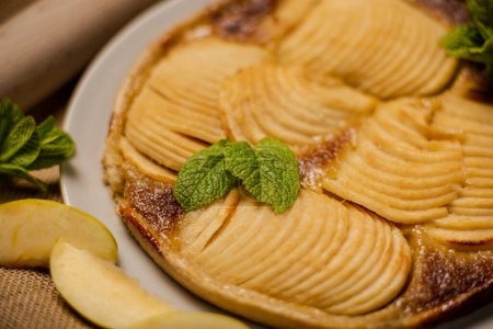 Téléchargez les photos : Tarte aux pommes française sur sa base feuilletée croustillante sont tranchées pommes juteuses mélangées avec de la cassonade, noix de muscade et d'autres épices. Décoré avec des feuilles de menthe. - en image libre de droit