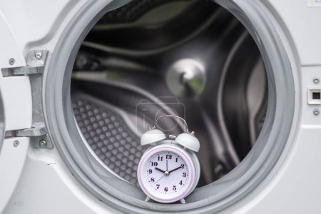 Zeit und Waschmaschine. Warten, Waschdauer-Konzept. Offene Tür von Waschmaschine und Wecker.