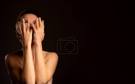 Photo for Amidst a black setting, a middle-aged woman sporting a short haircut obscures her face with her hands, reflecting negative emotions and a sense of depression - Royalty Free Image