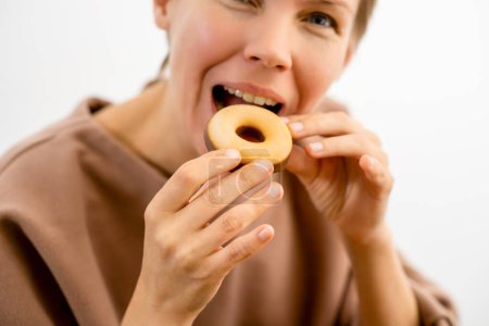 Foto de Disfrute de los placeres culpables: Una atractiva mujer de mediana edad disfrutando de un donut cubierto de chocolate - Imagen libre de derechos