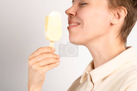 Una mujer en su mediana edad disfruta de un helado sobre un fondo blanco prístino, saboreando la delicia congelada con cada lamer deliciosa.