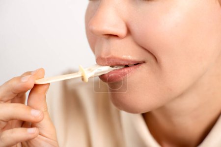 Großaufnahme einer nicht wiederzuerkennenden Frau, die ihr Eis auf einem Stock auf weißem Hintergrund beendet. Süßer Zahn, Dessert.