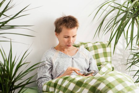A middle-aged woman spends her entire day in bed, staring at her phone. Emotional decay, laziness, doing nothing.