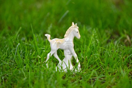ceramic white horse figurine on grass background.