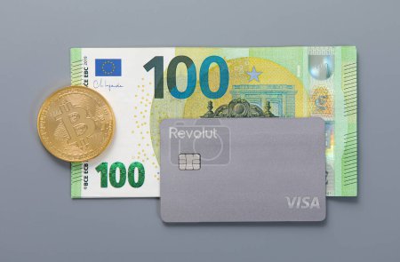 Photo for LONDON,UK - NOVEMBER 18, 2022: Revolut visa contactless card with bitcoin on grey with one hundred euro bill. Cryptocurrency and stock trading virtual banking.Top view - Royalty Free Image