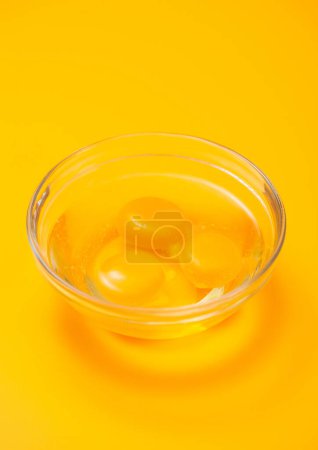 Téléchargez les photos : Trois jaunes d'oeuf dans une assiette de bol sur une table jaune. - en image libre de droit