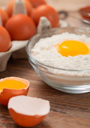 Photo for Bowl plate with flour and egg yolk on wooden table with fresh raw eggs - Royalty Free Image