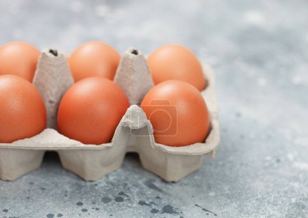 Foto de Huevos orgánicos crudos marrones en bandeja de papel sobre mesa de cocina ligera - Imagen libre de derechos