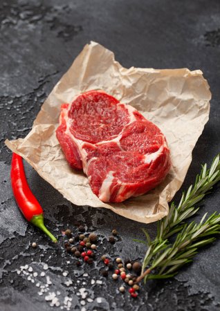 Photo for Fillet of raw rib eye steak with pepper,salt and rosemary on dark kitchen table background. - Royalty Free Image