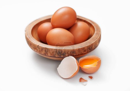 Foto de Brown fresh raw eggs in wooden bowl plate on white with shell and yolk - Imagen libre de derechos