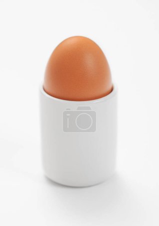 Foto de Brown raw egg in ceramic cup holder on white. - Imagen libre de derechos