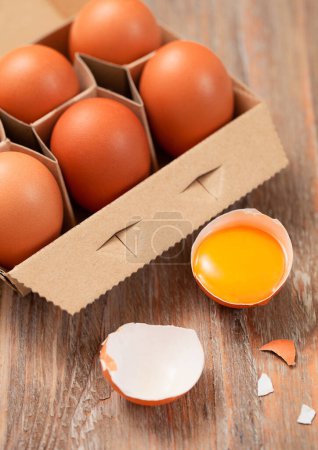 Photo for Brown raw farmers eggs in paper tray on light wooden table with yolk and shell - Royalty Free Image