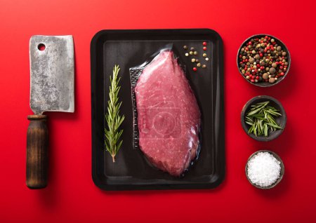 Photo for Fresh raw sirloin fillet steak with meat cleaver and rosemary,salt and pepper on red background.Top view. - Royalty Free Image
