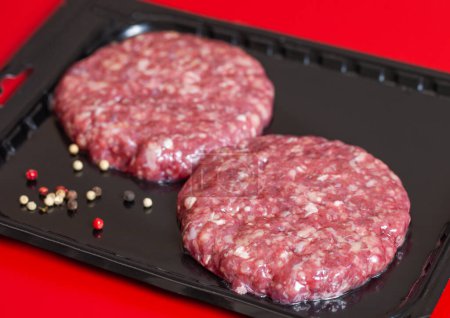 Foto de Raw minced beef burgers in plastick vacuum tray on red. - Imagen libre de derechos