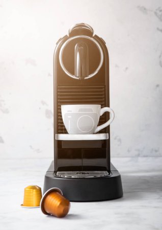 Téléchargez les photos : Home coffee machine with white cup and pods capsules on light kitchen background. - en image libre de droit