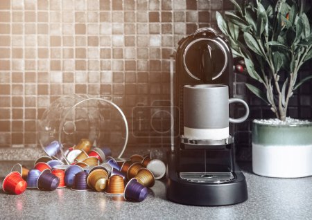 Téléchargez les photos : Home espresso machine with coffee cup and capsules on black kitchen background with olive plant - en image libre de droit