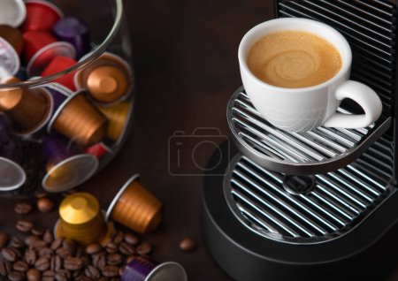 Foto de Cápsulas de cápsulas de cafetera con taza y granos de café de aroma crudo en marrón. - Imagen libre de derechos