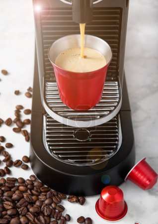 Foto de Taza de acero rojo con cápsulas de café y cafetera espresso casera en blanco con granos de café de aroma fresco. - Imagen libre de derechos