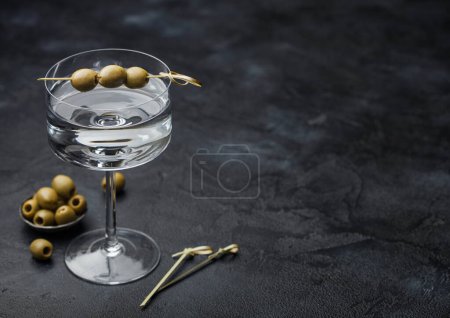 Téléchargez les photos : Cocktail de gin martini Vodka en verre moderne avec olives dans un bol en métal et bâtons de bambou sur fond noir. - en image libre de droit