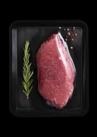 Photo for Fresh raw beef fillet steak sealed in vacuum tray with pepper and rosemary on black.Top view. - Royalty Free Image
