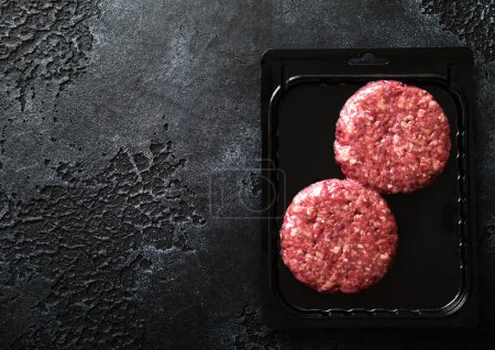 Photo for Raw minced beef burgers in plastic vacuum tray on black stone background.Top view - Royalty Free Image