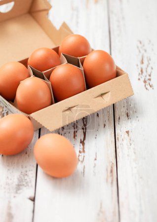 Foto de Huevos orgánicos frescos marrones en bandeja de papel sobre fondo de madera blanca. - Imagen libre de derechos
