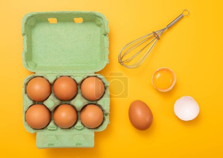 Foto de Bandeja verde con huevos marrones orgánicos con yema, batidor y cáscara en amarillo.Vista superior cincept. - Imagen libre de derechos