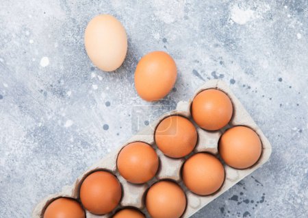 Foto de Huevos de granjeros crudos marrones en bandeja de papel sobre fondo de cocina claro. - Imagen libre de derechos