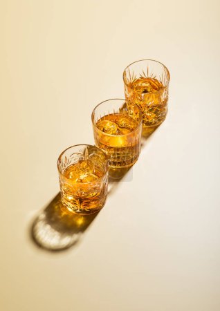 Photo for Crystal glasses of single malt whiskey with ice cubes on golden background.Top view. - Royalty Free Image