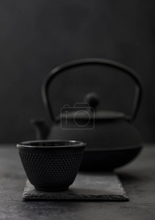 Photo for Chinese iron teapot with cup of traditional tea on black. - Royalty Free Image