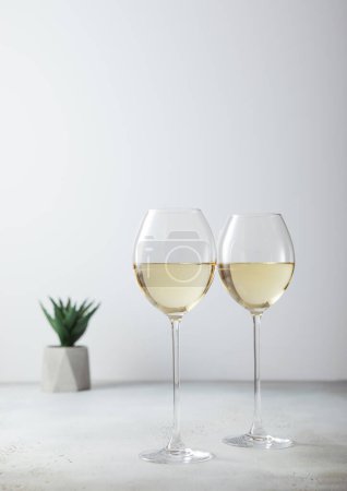 Photo for Glasses of white wine and small green flower on light board. - Royalty Free Image
