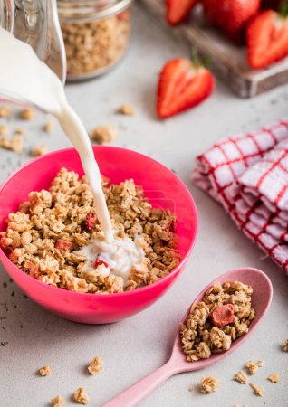 Photo for Pouring milk into bowl with strawberry granola on light board. - Royalty Free Image