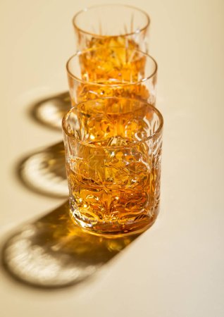 Photo for Crystal glasses of single malt whiskey with ice cubes on golden background. - Royalty Free Image