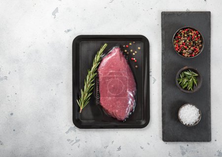 Photo for Raw beef fillet steak sealed in vacuum tray with pepper,salt and rosemary on light kitchen table background.Top view. - Royalty Free Image