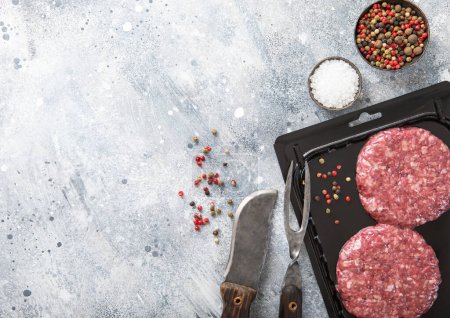 Photo for Beef fresh raw burgers in vacuum tray with fork and knife on light background with salt and pepper.Top view. - Royalty Free Image
