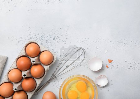 Foto de Huevos marrones orgánicos con yema, batidor y cáscara en mesa de cocina ligera. - Imagen libre de derechos