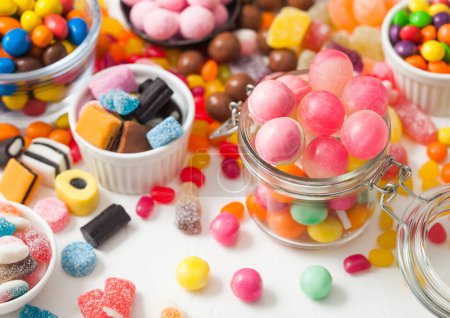 Photo for Pink lollipop candies in jar with various milk chocolate and jelly gums candies on white with liquorice allsorts and strawberry bonbons - Royalty Free Image
