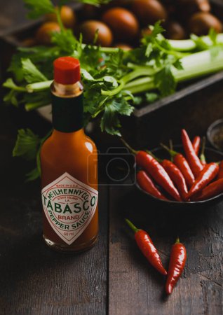 Photo for LONDON, UK - MARCH 22, 2023: Tabasco red pepper sauce bottle on wooden background with red peppers and celery.Top view. - Royalty Free Image