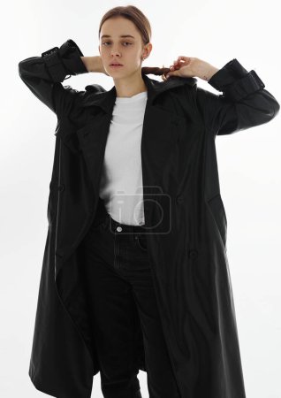 Téléchargez les photos : Mode jeune beau modèle en long manteau en cuir et jean foncé sur blanc. - en image libre de droit
