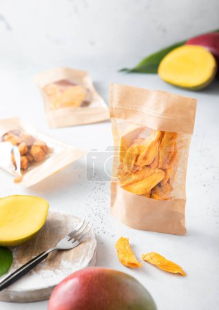 Téléchargez les photos : Différents paquets avec des morceaux de mangue séchés doux et des boules sur un tableau de cuisine léger. - en image libre de droit