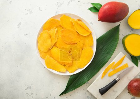 Téléchargez les photos : Assiette avec tranches de mangue sucrée séchées avec planche à découper et couteau.. - en image libre de droit