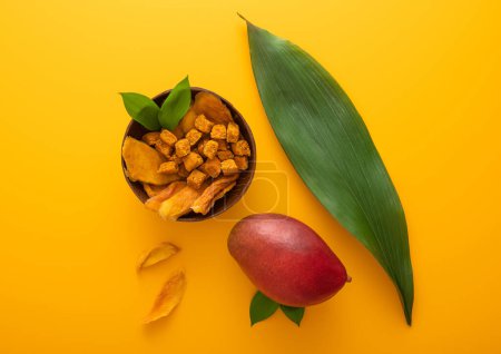 Téléchargez les photos : Tranches et boules séchées à la mangue dans une assiette à bol sur fond jaune.. - en image libre de droit