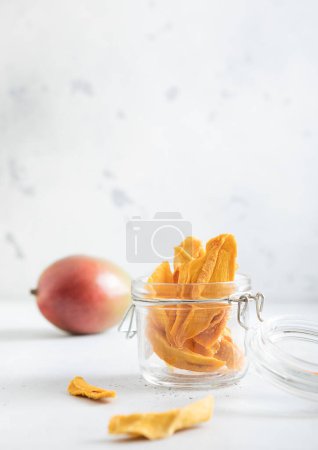 Téléchargez les photos : Morceaux de mangue séchés dans un bocal en verre et fruits crus sur fond clair. - en image libre de droit