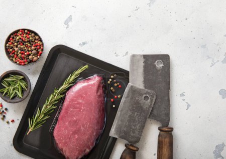 Téléchargez les photos : Bifteck de filet cru de boeuf dans un plateau à vide avec des couteaux à viande sur fond clair avec du sel et du poivre.. - en image libre de droit