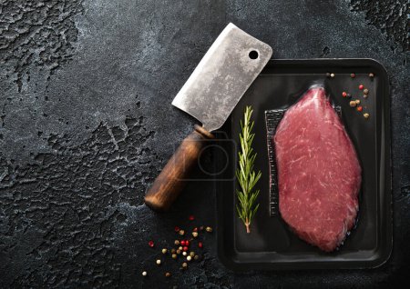Photo for Raw sirloin ribeye fillet steak with meat cleaver and rosemary with pepper on black background.Top view. - Royalty Free Image