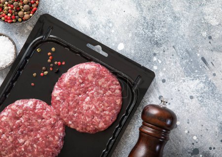 Photo for Beef fresh raw organic burgers in vacuum tray with pepper grinder on light kitchen table background.Top view. - Royalty Free Image